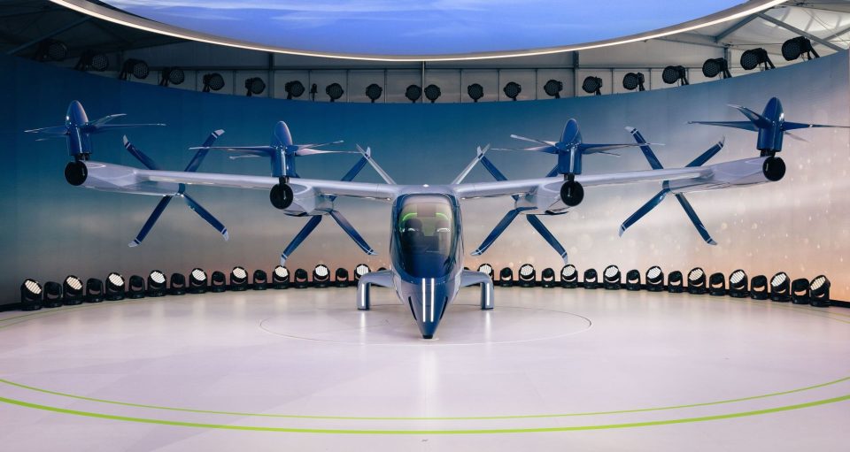 Aeronave elétrica eVTOL futurista, com hélices, exposta em ambiente interno.