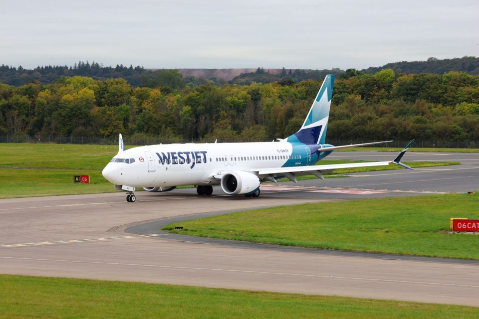 Avião da WestJet taxiando em uma pista de aeroporto, cercado por área verde.