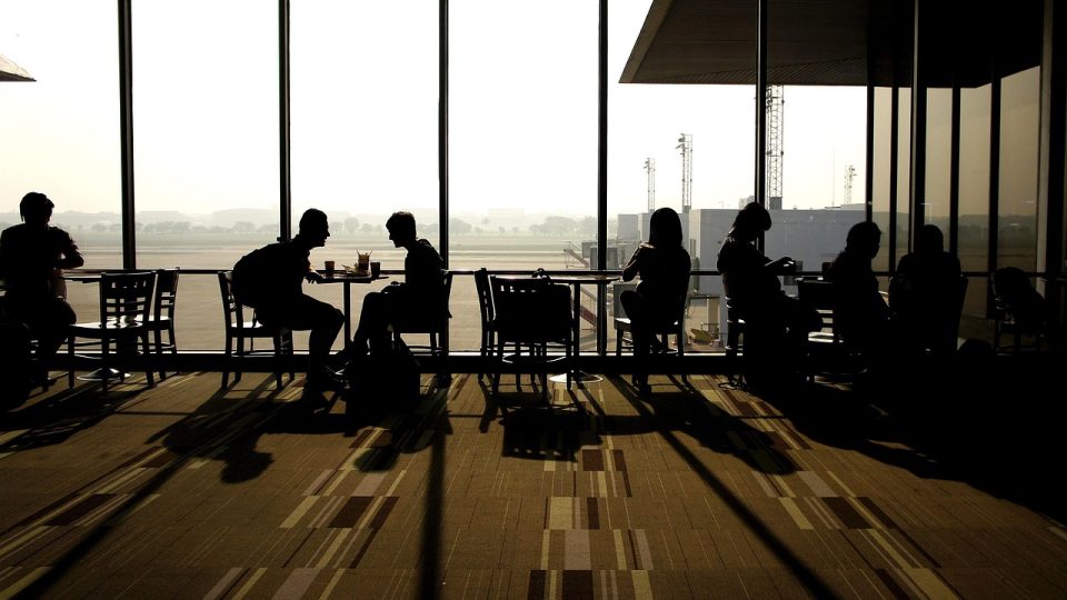 Área de espera tranquila em um aeroporto, com mesas e assentos junto a uma janela.