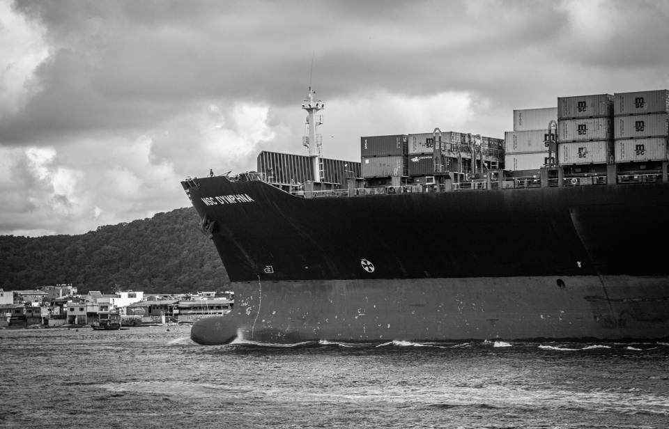 Navio porta-contêineres atracado no Porto de Santos, com estruturas portuárias ao redor.